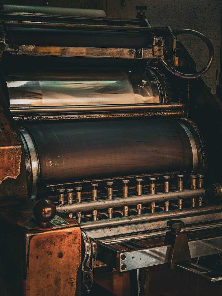 照片由 Salem Raju 拍摄 Close-up view of an old printing press showcasing rollers and gears, emphasizing industrial mechanics.